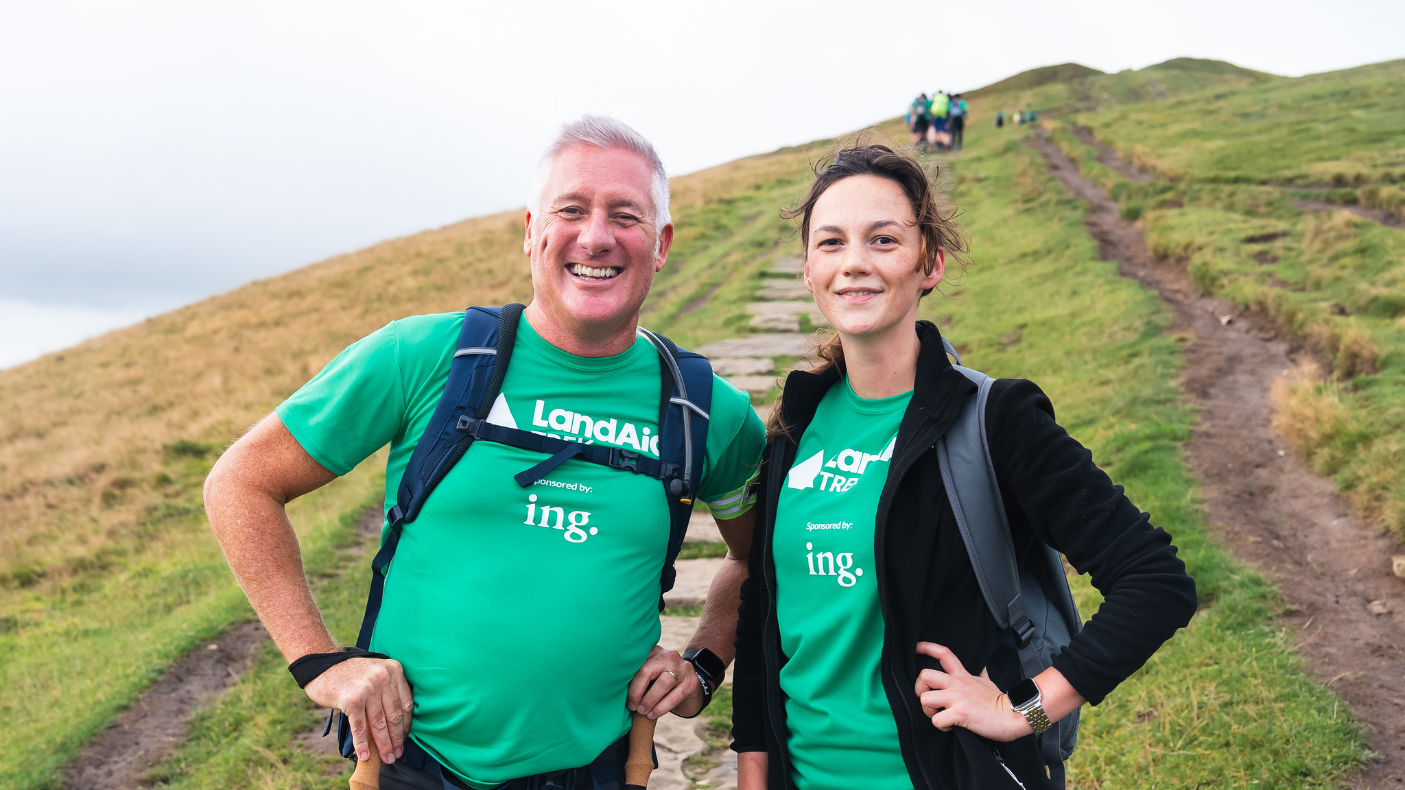 mand and a woman stood together smiling with a hill top view in the background.